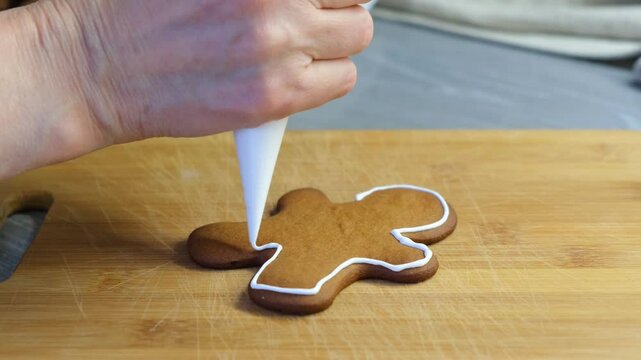 Hands of woman decorating gingerbread cookie with icing bag. High quality 4k footage