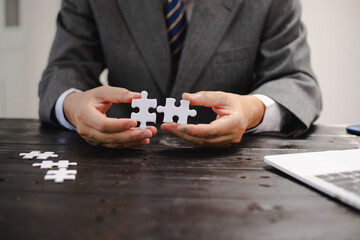 Businessman sitting at a table intently completing a jigsaw puzzle, demonstrating problem-solving, strategic thinking, and business decision-making, as well as attention to detail and patience.