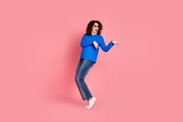 Young woman in blue sweater posing playfully against pink background, showcasing fashion and confidence in casual style