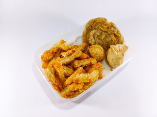 Slices of chicken katsu and pempek, a savory Indonesian fishcake delicacy, arranged in a transparent container, showcasing a fusion of crispy chicken and flavorful fishcake in a convenient display