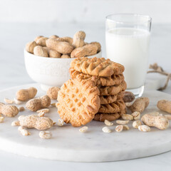 A stack of peanut butter cookies with a glass of milk and peanuts all around.