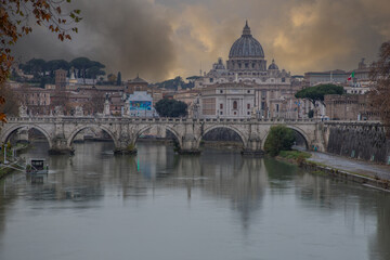 View over the Tiber River in a historic city. The old well-known bridge Ponte Sant'Angelo, in the evening. Rainy weather at sunset and view of the Basilica di San Pietro, Rome, Italy