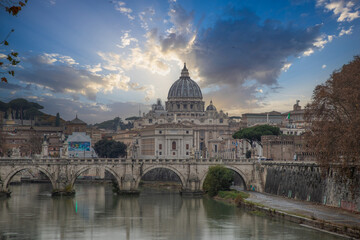 View over the Tiber River in a historic city. The old well-known bridge Ponte Sant'Angelo, in the evening. Rainy weather at sunset and view of the Basilica di San Pietro, Rome, Italy