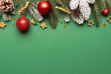 Bright festive Christmas border with fir tree branches, shining decorations and red balls on beautiful green background top view, copy space for your design.