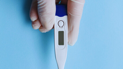 Hand holding digital thermometer on blue background