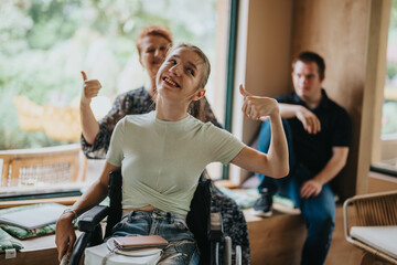 A cheerful young woman in a wheelchair giving a thumbs up, surrounded by friends indoors. The image conveys positivity, inclusion, and friendship.