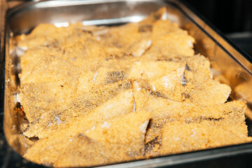Close-up of cornmeal-crusted fish fillets in baking tray highlighting culinary preparation