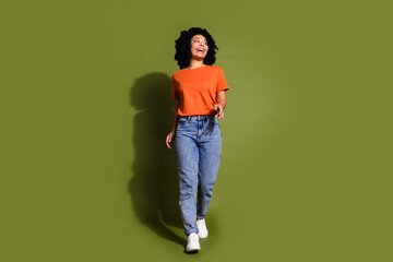 Full size photo of pretty young girl walking look empty space wear trendy orange outfit isolated on...