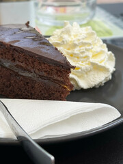 Decadent chocolate cake slice with fresh whipped cream on black plate
