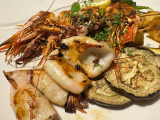 Grilled seafood platter with squid, shrimp, and eggplant on a white plate