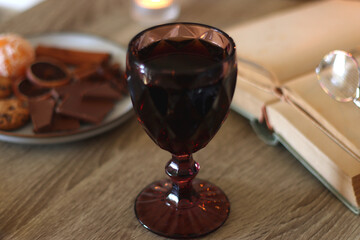 Books, lit candles, red wine, snacks and various deocration on the table. Dark academia or Halloween concept. Selective focus.