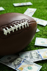 Obraz premium American football ball and dollar banknotes on green grass outdoors, closeup
