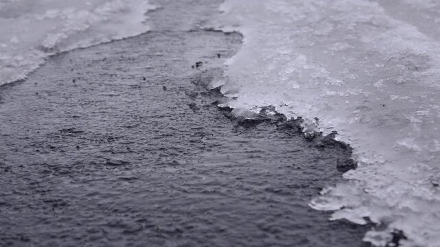 道路と氷の間にできた隙間を流れる水　雪解けイメージ