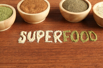 Word Superfood and different healthy powders on wooden table, closeup