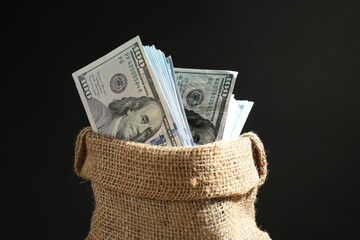 Dollar banknotes in burlap sack against black background, closeup