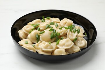 Delicious pelmeni with green onion in bowl on light table, closeup