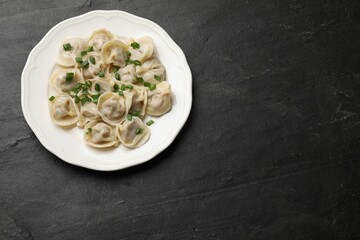 Delicious pelmeni with green onion on grey textured table, top view. Space for text
