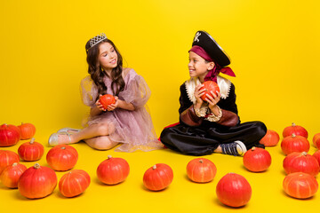 Full body portrait of two kids halloween princess pirate costume sit floor hold pumpkin isolated on yellow color background