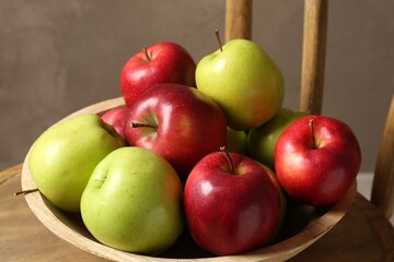 Ripe red and green apples in bowl on chair near grey wall, closeup