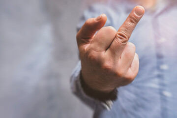 Man in a shirt showing a crude fuck gesture, middle finger sign, close-up against a concrete wall.