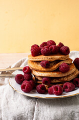 Delicious whole wheat healthy pancakes with raspberry, fork and knife styling natural light and copy space on the table with linen cloth background lifestyle