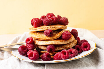 Delicious whole wheat healthy pancakes with raspberry, fork and knife styling natural light and copy space on the table with linen cloth background lifestyle