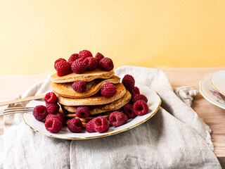 Delicious whole wheat healthy pancakes with raspberry, fork and knife styling natural light and copy space on the table with linen cloth background lifestyle