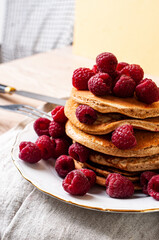 Delicious whole wheat healthy pancakes with raspberry, fork and knife styling natural light and copy space on the table with linen cloth background lifestyle