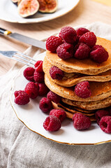 Delicious whole wheat healthy pancakes with raspberry, fork and knife styling natural light and copy space on the table with linen cloth background lifestyle