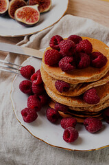 Delicious whole wheat healthy pancakes with raspberry, fork and knife styling natural light and copy space on the table with linen cloth background lifestyle