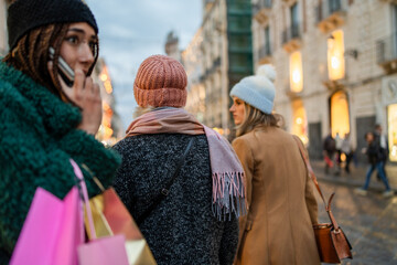 Diverse women friends shopping in winter city street at dusk