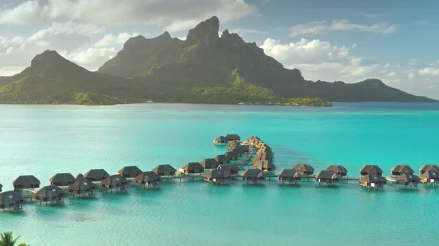 Aerial view overwater bungalows forming line towards mount Otemanu on tropical exotic Bora Bora island, with its turquoise lagoon and lush vegetation. Luxury travel vacation resort in coral reef ocean