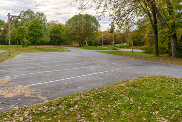 Empty parking lot in a public park surrounded by woodland under cloudy sky at sunset in autumn