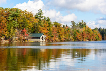 Wooden boathouse on a lake surrounded by woodland at the peak of fall foliage on a sunny day