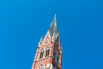 Majestic church Herz Jesu Kirche in Graz, Styria, Austria. Landmark against clear blue sky. Intricate architectural details, including pointed spire, ornate windows, clock face. Gothic architecture