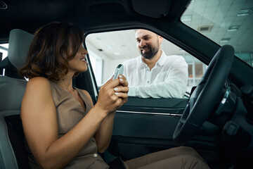 Happy young woman holding key sitting in her new car