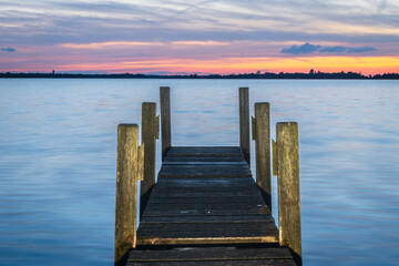 Fototapeta premium Beautiful blue and orange sunset with wooden dilapidated Jetty stretching out over the water surface