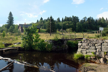 Fototapeta premium rural landscape with an old wooden house and a bridge over the river, Karelia