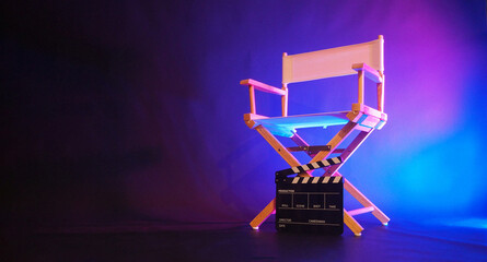 Director chair and black clapper board in blue purple light.