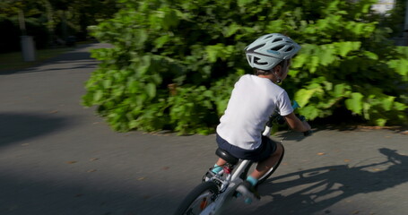 Young boy crossing a crosswalk on his bicycle, wearing a helmet for safety, in an urban setting with trees and street signs, enjoying outdoor activity on a sunny day