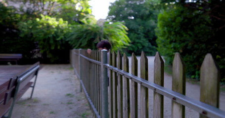 Fototapeta premium Young boy leaning over a wooden fence, wearing a white shirt, curiously looking into the distance, surrounded by greenery, enjoying an outdoor exploration on a sunny day