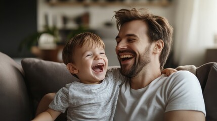 Father and young son laughing together on the couch, enjoying morning playtime. Simple home setting, emphasizing support and family care.