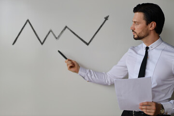 A man is standing in front of a whiteboard with a graph on it. He is holding a marker and pointing...