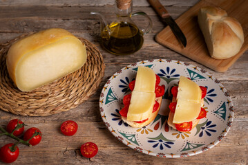 Cow's milk cheese from Mallorca on slices of bread with cherry tomatoes, next to a square piece of cheese, cherry tomatoes, oil and bread, close-up.