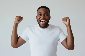 Fototapeta premium A Happy Young Man Celebrating Success in a Plain White T Shirt Against a Light Grey Background, Expressing Joy and Excitement With a Broad Smile and Raised Fists