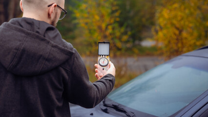 Man Using a Compass to Navigate Near a Parked Car in a Forested Area During Autumn