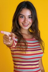 A young girl smiles and points at the camera, making eye contact