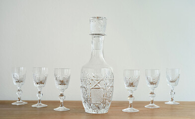 Elegant empty bottle and small crystal glasses with high stem on the brown wooden table. Close-up. Copy space. Selective focus.