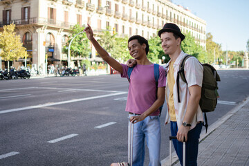 Obraz premium A multiethnic couple of two young men stand on the street raising their hands to hail a cab.