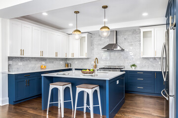 A luxurious white and blue kitchen with gold hardware, stainless steel appliances, and white...